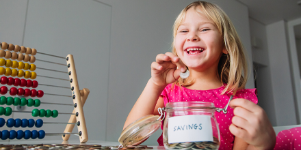 Happy child putting coins into jar labeled savings